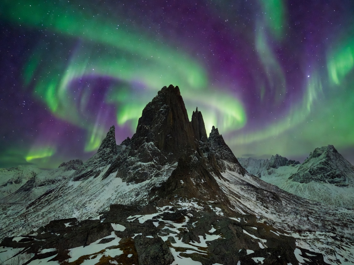 The jagged rock towers of Okshornan in Senja Norway under purple and green auroral ribbons